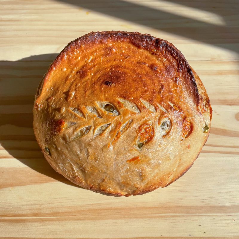 Jalapeño cheddar sourdough boule, scored with the green pieces showing